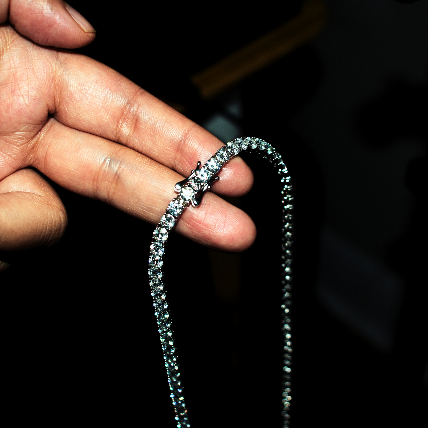 Hand holding an iced out moissanite tennis chain showcasing VVS clarity stones and secure clasp detail.